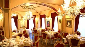 Une salle à manger élégante, avec des tables rondes, des chaises recouvertes de tissu rouge et de magnifiques lustres.