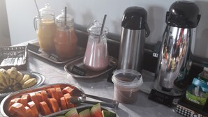 Un buffet de petit-déjeuner proposant une variété de fruits, de jus de fruits et une machine à café.