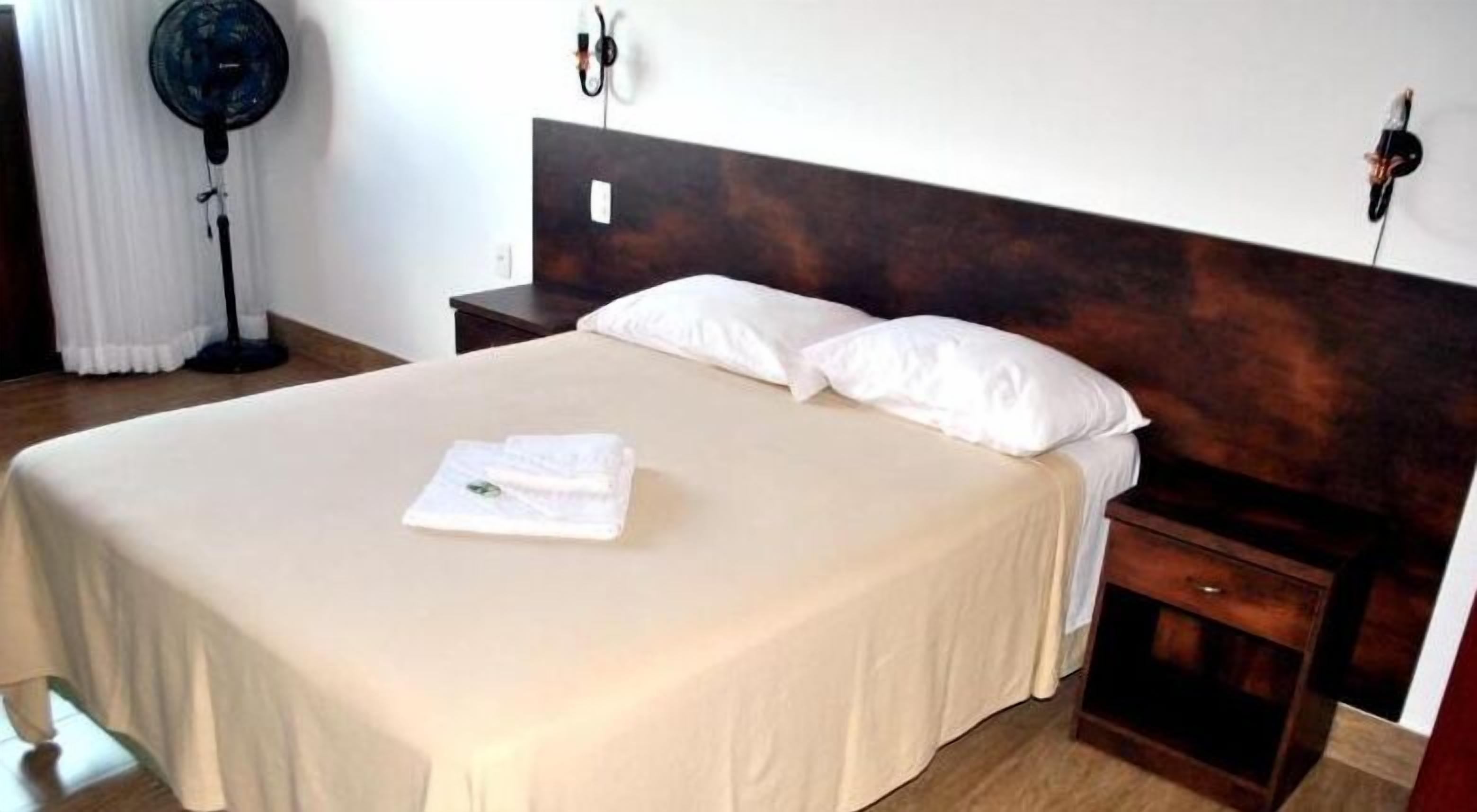 A neatly made bed with white linens and pillows, a bedside table with a lamp, and a dark wooden headboard.