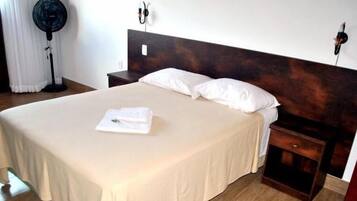 A neatly made bed with white linens and pillows, a bedside table with a lamp, and a dark wooden headboard.