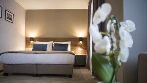 Ein Hotelzimmer mit einem großen Bett, zwei Nachttischlampen, einem Nachttisch und einer Orchidee im Topf.