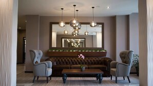 Eine moderne Lobby mit einem gepolsterten Ledersofa, zwei Sesseln, einem Marmortisch und einem großen Spiegel über dem Sofa.