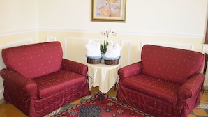 A room with two red upholstered armchairs, a small table with two wicker baskets containing folded white towels, and a painting on the wall. - Hotel Palazzo Krataiis (Scilla)