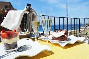 A table with a dessert, two glasses of champagne, and a spoon on a yellow tablecloth with a coastal view.