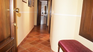 A hallway with a wooden door, tiled floor, and a bench. - Hotel Palazzo Krataiis (Scilla)