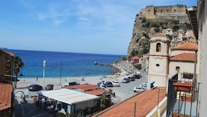 A coastal town with a historic fort, a beach, and parked cars along the road. - Hotel Palazzo Krataiis (Scilla)