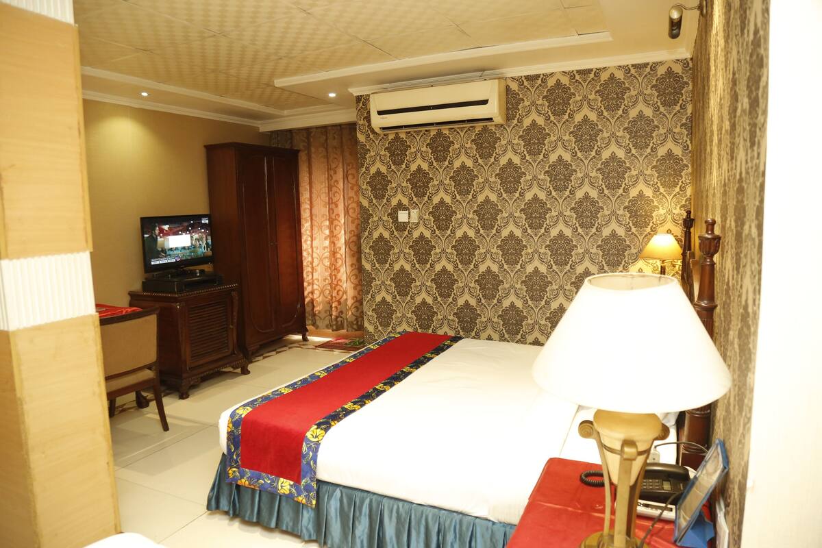 Una habitación de hotel con cama, televisión, escritorio y aire acondicionado.