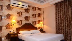 A neatly made bed with a wooden headboard, two bedside lamps, and a wall air conditioner. - Sea Shell Residence (Dhaka)