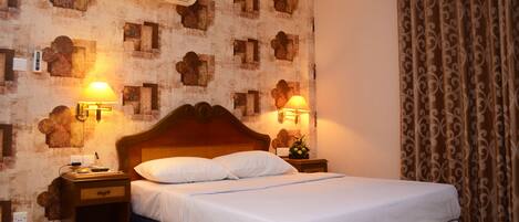 A neatly made bed with a wooden headboard, two bedside lamps, and a wall air conditioner.