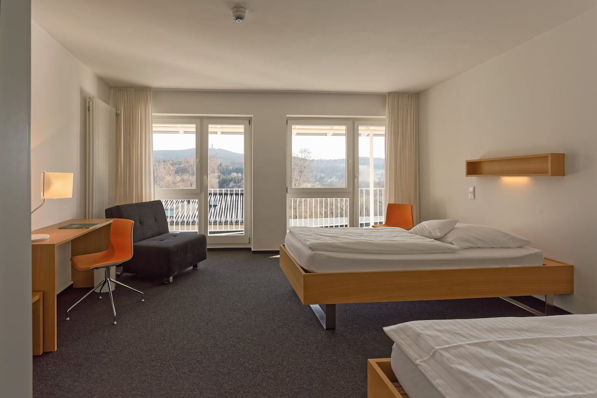 A hotel room with a bed, a desk, a chair, and a view of the outdoors.