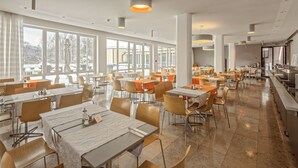 Uma sala de jantar ampla, com várias mesas e cadeiras, grandes janelas e um design de teto moderno.