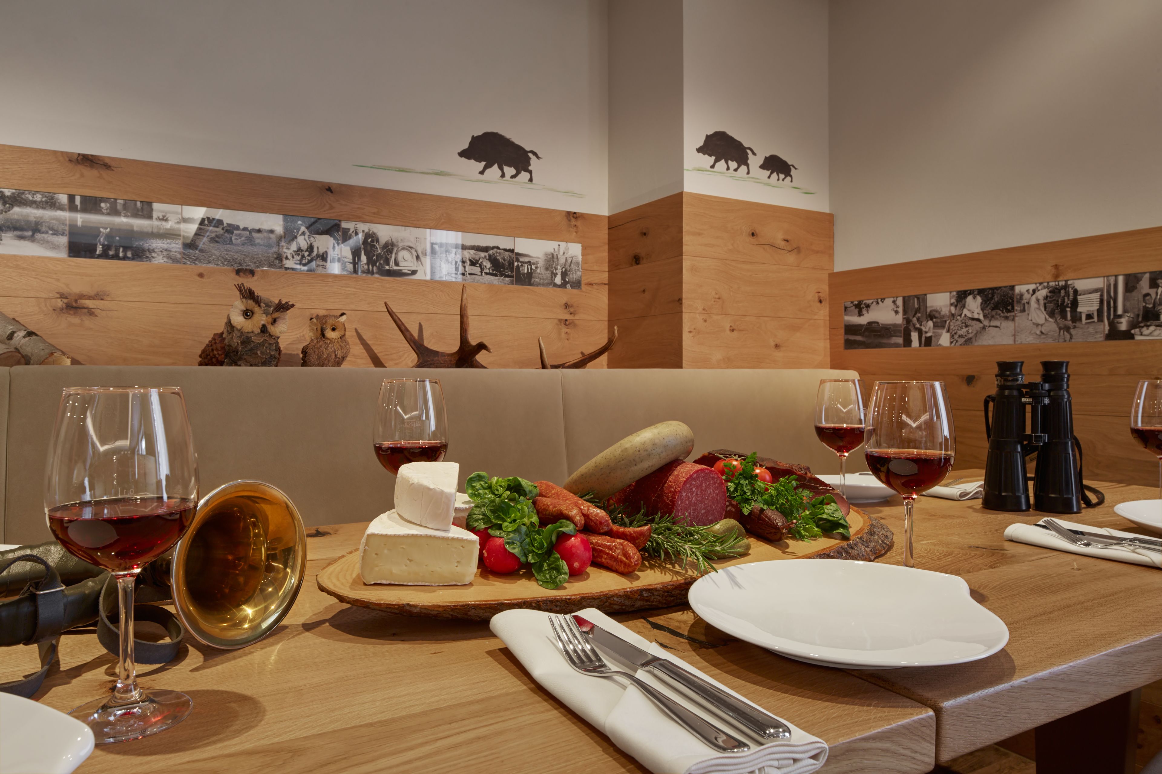 A dining table with a cheese platter, wine glasses, and a wooden wall with animal silhouettes.