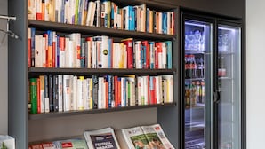 A book store with shelves of books and a refrigerator with beverages. - Trip Inn Jet Hotel Zürich Airport (Ruemlang)