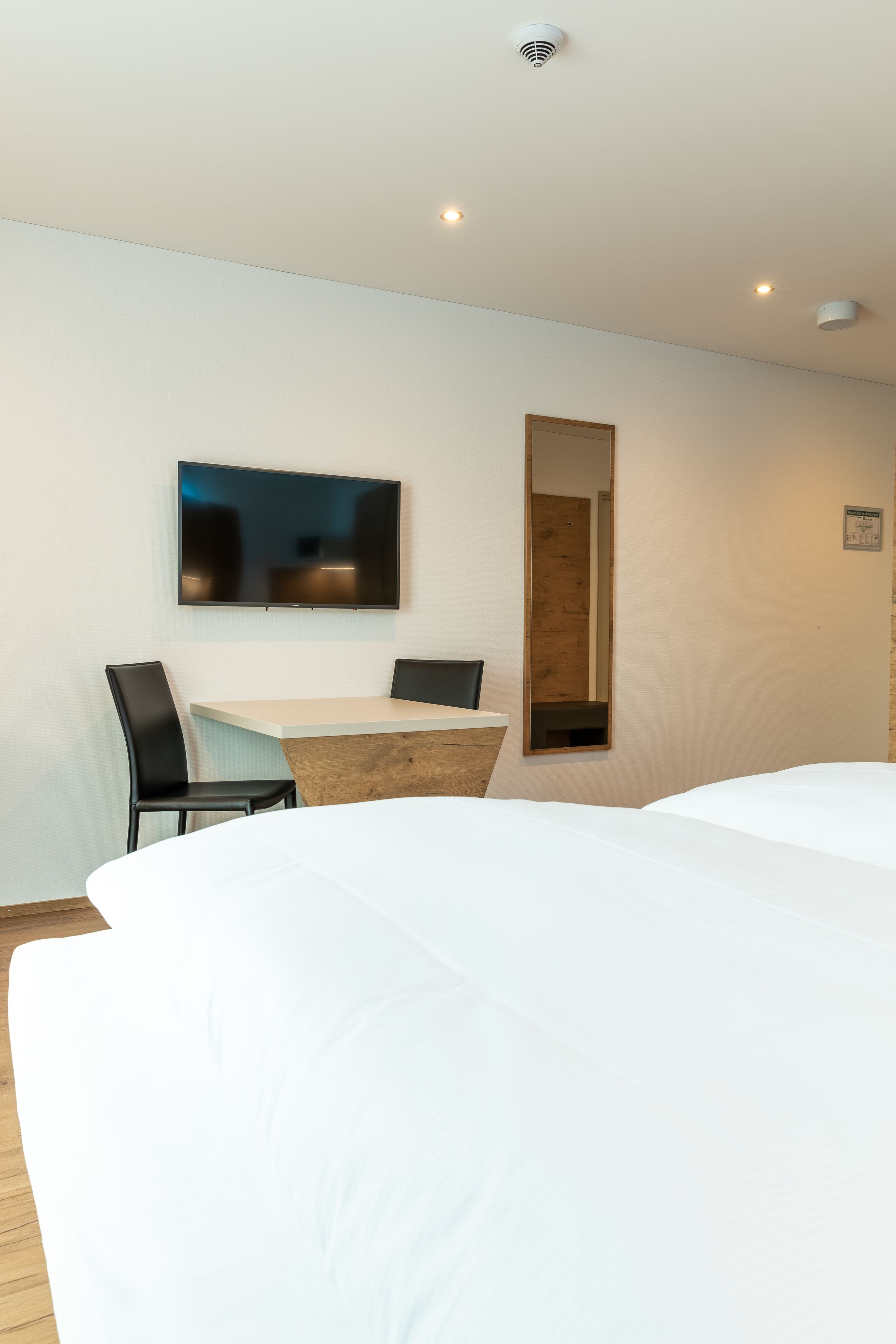 Ett modernt hotellrum med en stor säng, ett skrivbord med två stolar, en platt-TV och en spegel.