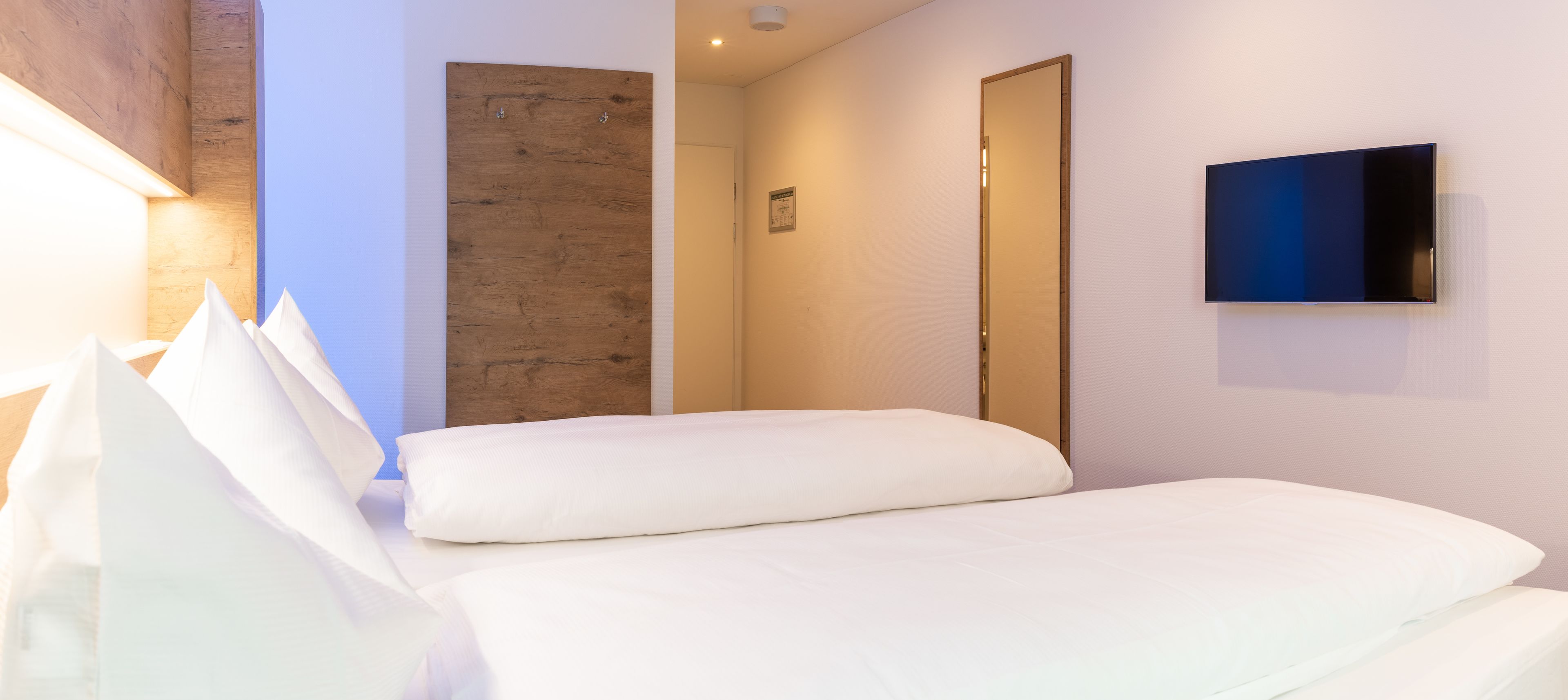 Une chambre d’hôtel avec un lit, un mur décoratif en bois, une porte et un téléviseur à écran plat fixé au mur.