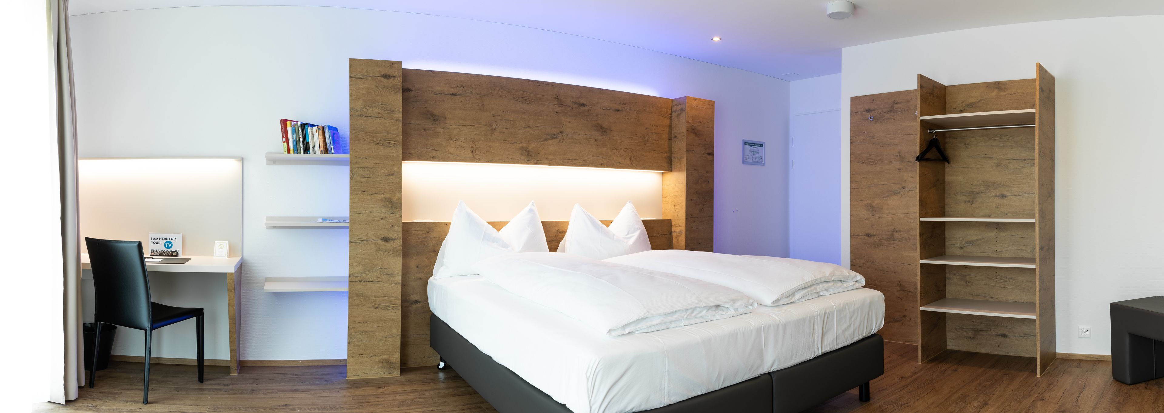 Ein modernes Hotelzimmer mit einem Bett, einem Schreibtisch und einem Kleiderschrank.