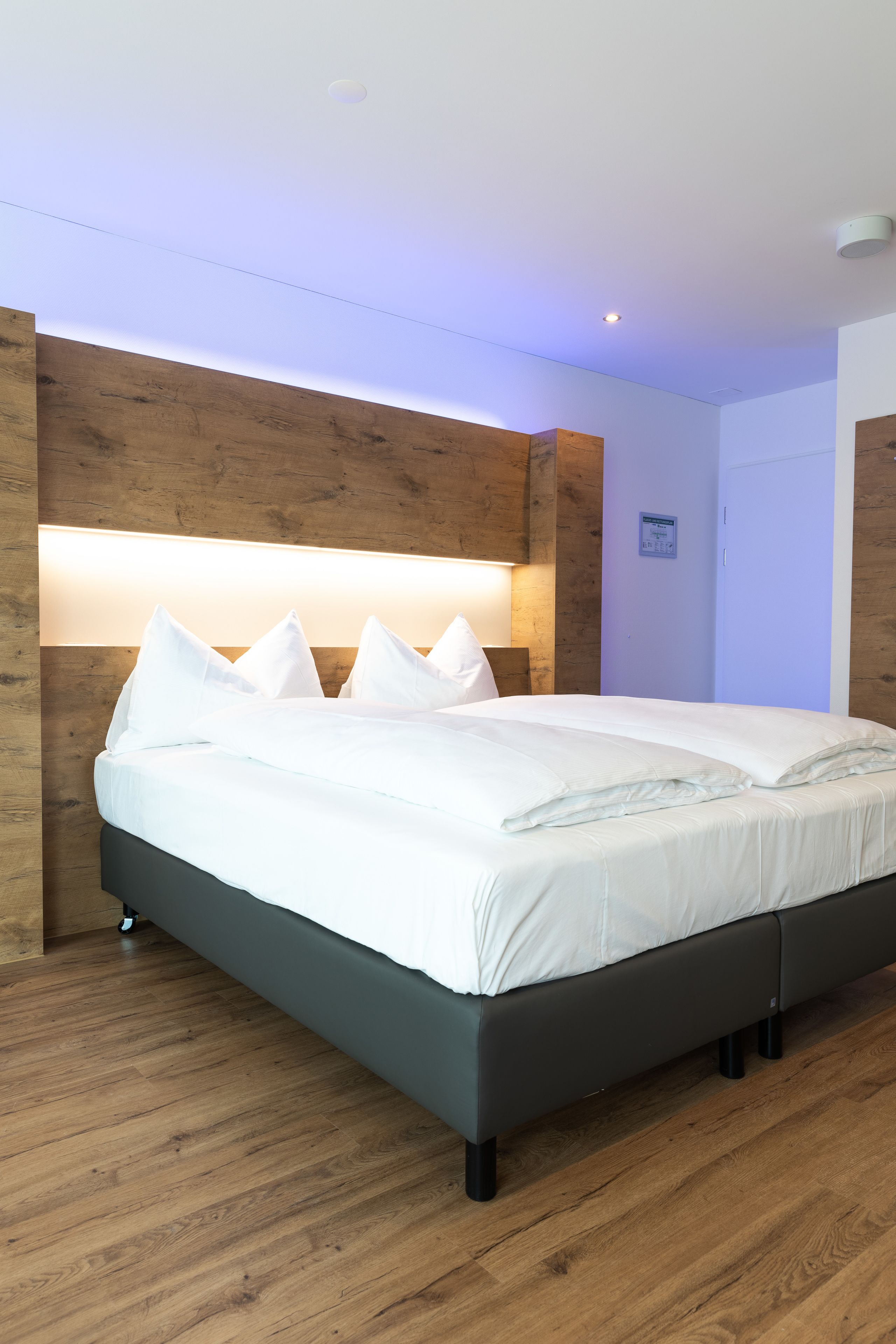 Ein modernes Hotelzimmer mit einem großen Bett, einem Holz-Kopfteil und einer Wandleuchte.