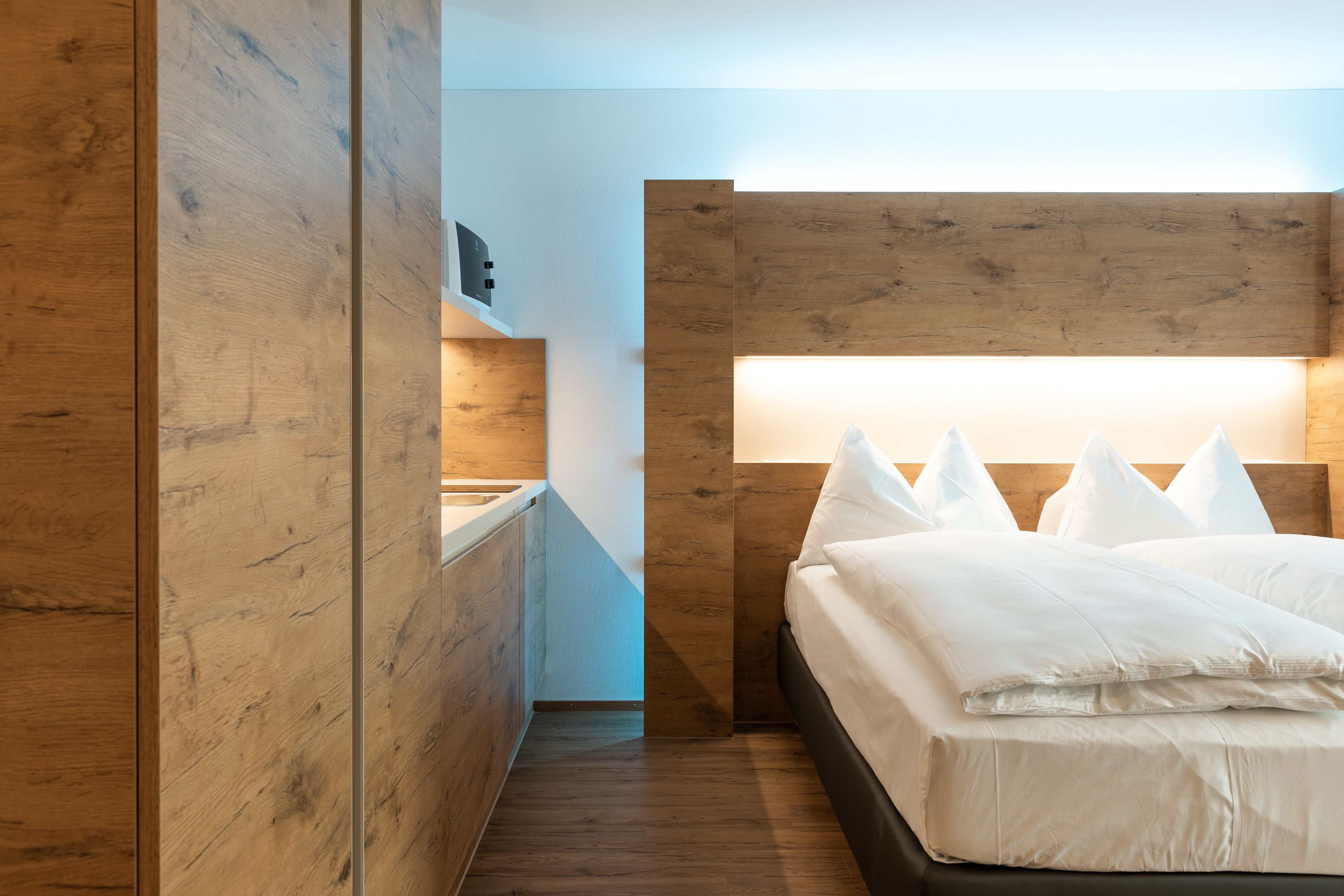 Un dormitorio moderno con cabecera de madera, una mesita de noche y una cama con ropa de cama blanca.