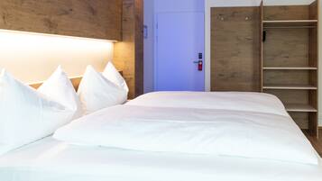 A neatly made bed with white linens and pillows, a wooden headboard, and a wooden wardrobe with open doors.