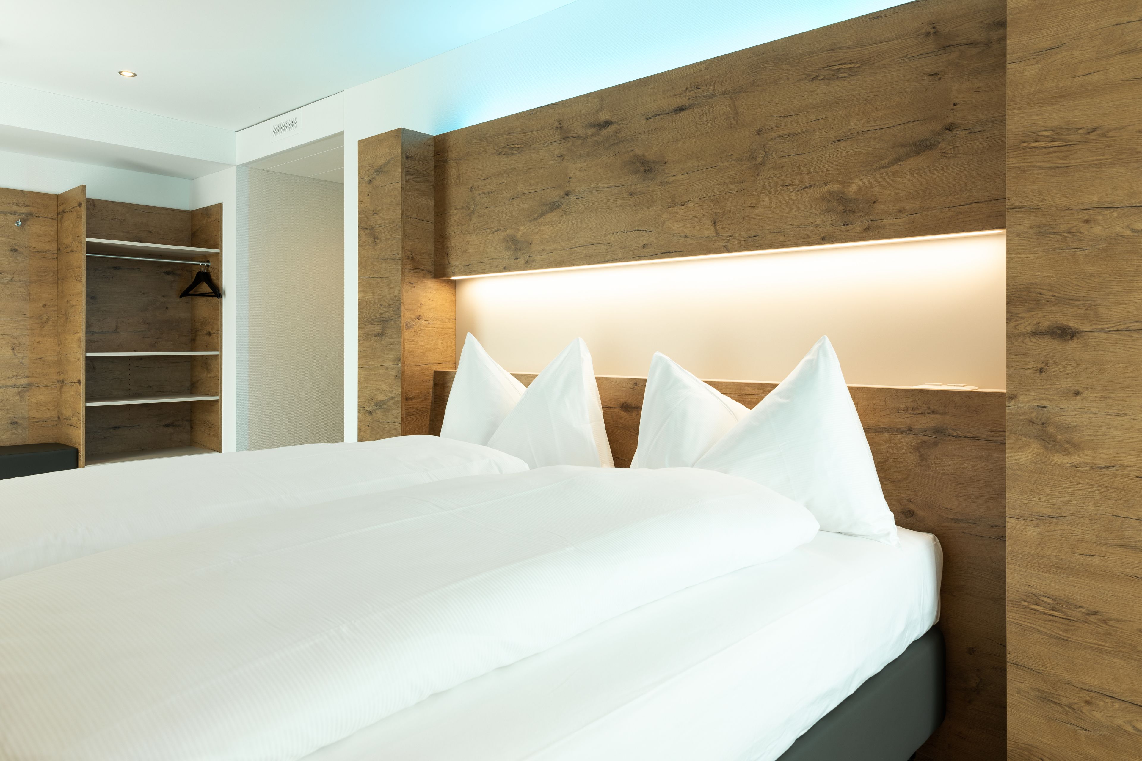 Una moderna camera d'albergo con un letto grande, una testiera in legno e un armadio a muro.