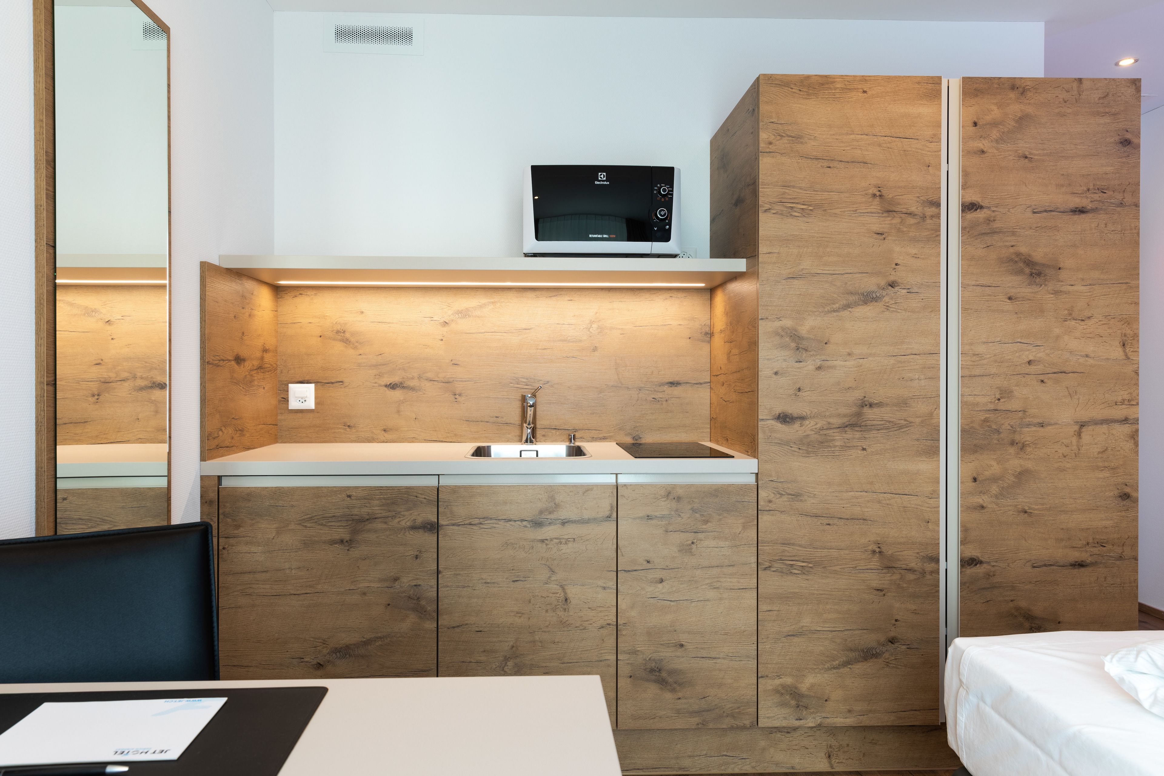 Une cuisine moderne équipée d’un four à micro-ondes encastré, d’un évier et de meubles de rangement en bois.