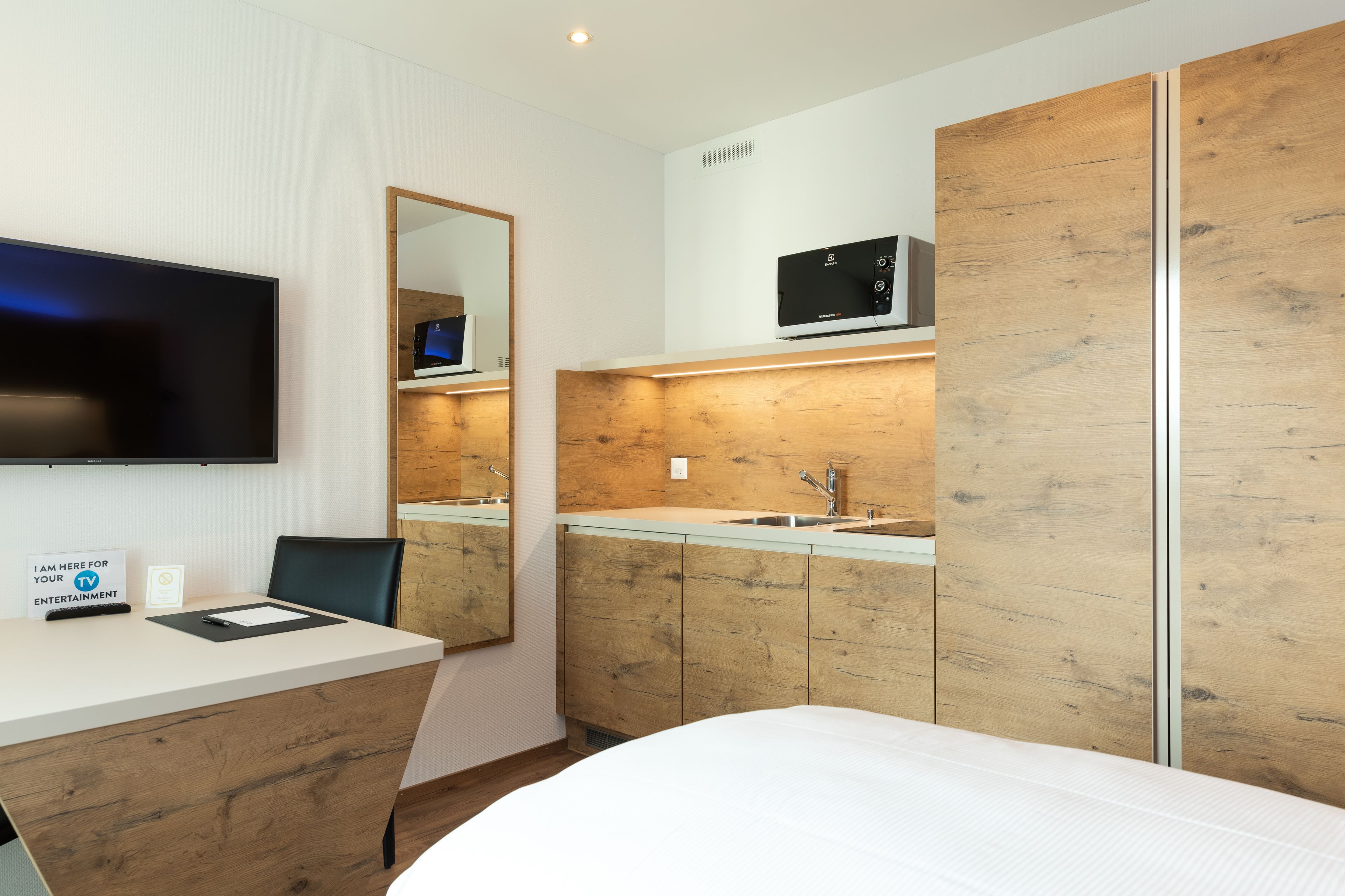 A modern hotel room with a wooden vanity, a flat-screen TV, and a microwave.