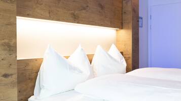 Una camera d'albergo moderna con una testiera in legno, un letto grande con biancheria bianca e una lampada a sospensione luminosa.