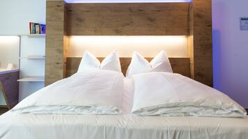 A neatly made bed with white bedding and pillows, a wooden headboard, and a white nightstand with books.