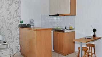 A compact kitchen with wooden cabinets, a built-in sink, and a small dining area with stools.