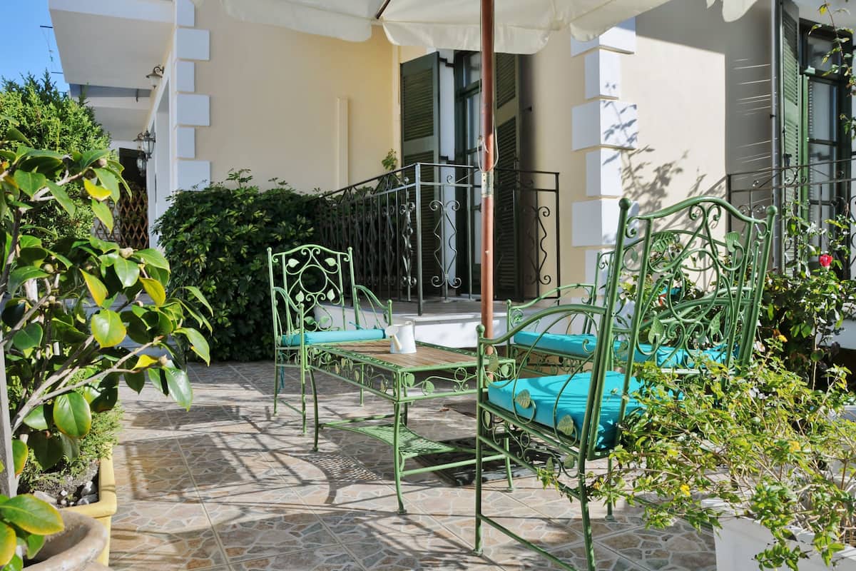 Eine Terrasse mit grünen Metallmöbeln, einem weißen Sonnenschirm und einem Boden aus Steinplatten.