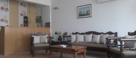 Una sala de estar con un sofá, dos sillones, una mesa de centro de madera, un reloj y un cuadro en la pared.