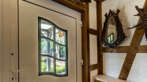 A room with a white door featuring a window with multiple panes, a wooden bench with a mirror, and exposed wooden beams on the ceiling. - Ferienhaus Stift Ennenbach (Ruppichteroth)