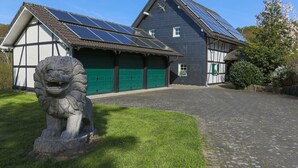 A traditional building with solar panels, a green garage, and a stone lion statue. - Ferienhaus Stift Ennenbach (Ruppichteroth)