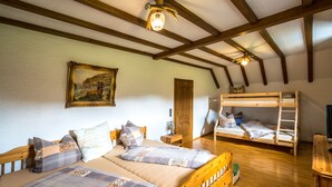 A room with two wooden beds, a bunk bed, wooden beams on the ceiling, a painting on the wall, and a wooden floor. - Ferienhaus Stift Ennenbach (Ruppichteroth)