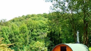A rustic wooden structure with a green roof, surrounded by lush greenery and a wooden bench area. - Ferienhaus Stift Ennenbach (Ruppichteroth)