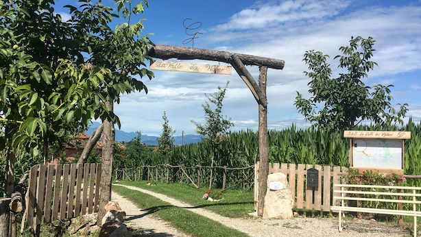 Ein rustikaler hölzerner Bogen mit dem Schild "La Valle dei Vigner“, der zu einem Schotterweg führt.