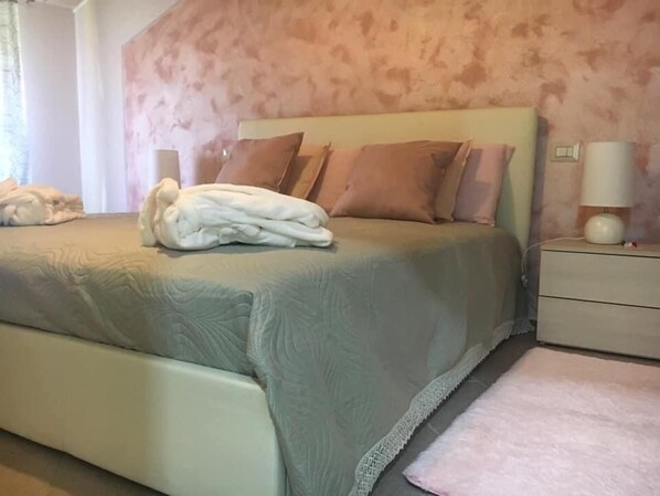 A neatly made bed with a folded white towel, a bedside lamp, and a nightstand with a lamp. - B&B La Valle Dei Vigher (Cavriana)