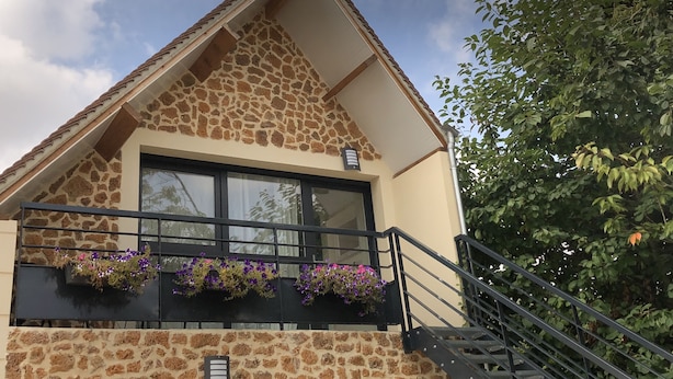 A building with a stone facade, a large window, and a balcony with flower boxes. - Chambre d'hôtes La Bourdonnaise (Bourdonne)