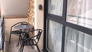 A balcony with a table and chairs, a glass door with a patterned curtain, and a stone-tiled floor. - Chambre d'hôtes La Bourdonnaise (Bourdonne)