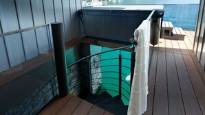 Una terraza de madera con un jacuzzi, balaustrada de vidrio y vista al agua.