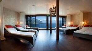 Una habitación con cuatro tumbonas, ventanas amplias que dan a vistas de montañas y un candelabro.