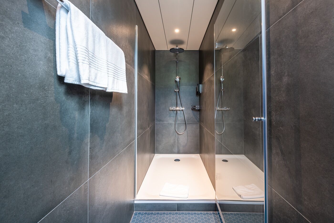 A modern shower area with a glass partition, a handheld showerhead, and a wall-mounted faucet.