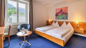 Ein Hotelzimmer mit Bett, Sessel, kleinem Tisch und Fenster mit Bergblick.