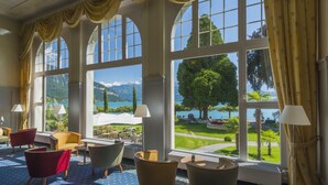 Un vestíbulo de hotel con amplias ventanas de arco, varias zonas de estar y vistas a un jardín ajardinado y montañas.