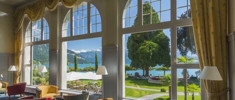 A hotel lobby with large arched windows, multiple seating areas, and a view of a landscaped garden and mountains.
