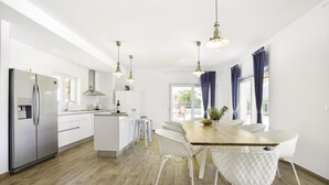 Een moderne keuken met witte kastjes, een roestvrijstalen koelkast en een houten eettafel met witte stoelen.