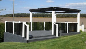 A covered outdoor area with a white structure and black roof, surrounded by a white fence and a grassy lawn. - Broomlea (Inverness)