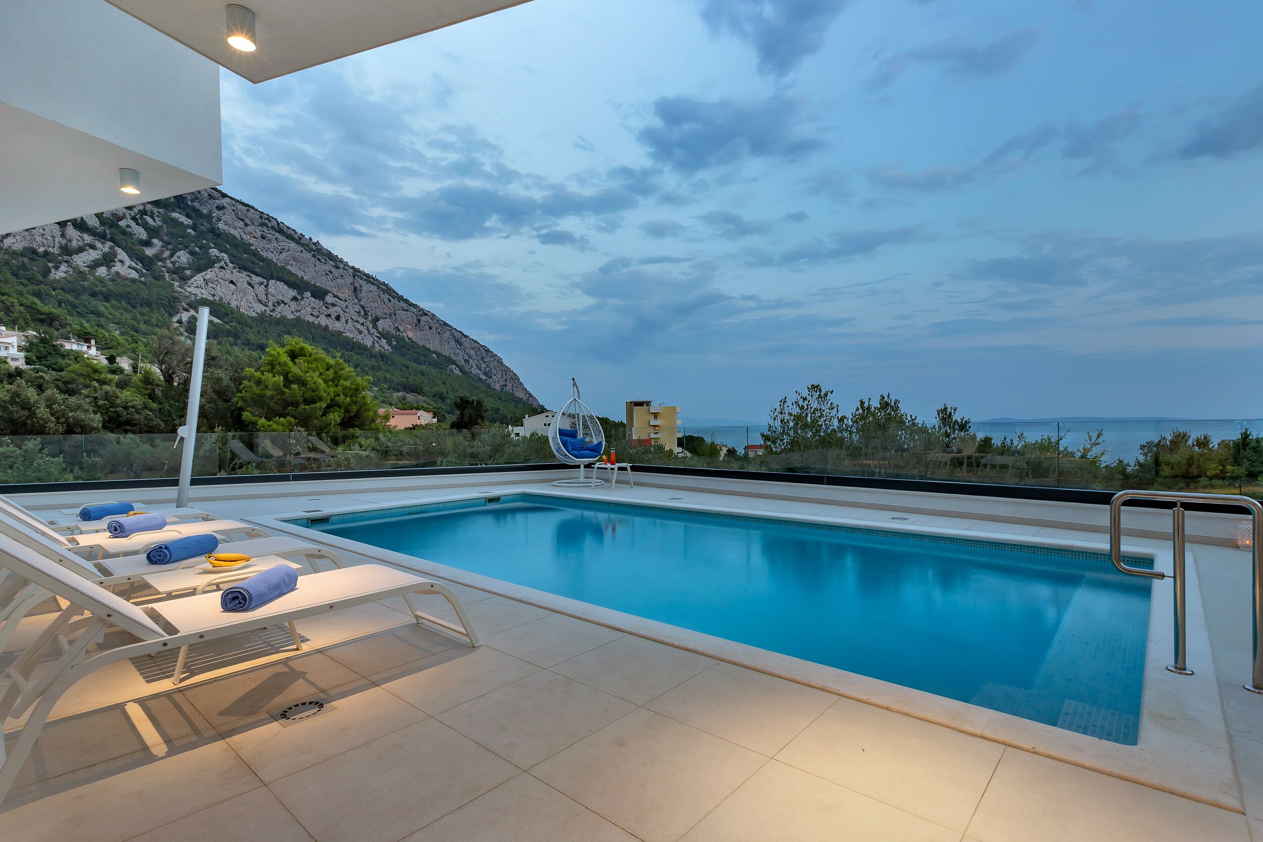 A swimming pool with lounge chairs and a view of the sea and mountains.