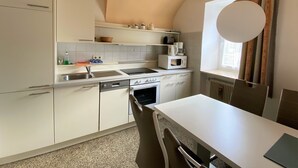 Cuina compacta amb armaris blancs, forn de microones integrat i finestra amb cortines.