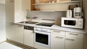 Una cuina compacta amb armaris blancs, forn integrat, microones, cafetera i una estant amb menjar i utensilis de cuina.